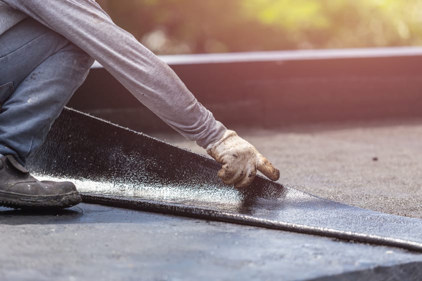 Entrepreneur qualifié RBQ posant une membrane élastomère sur toit plat