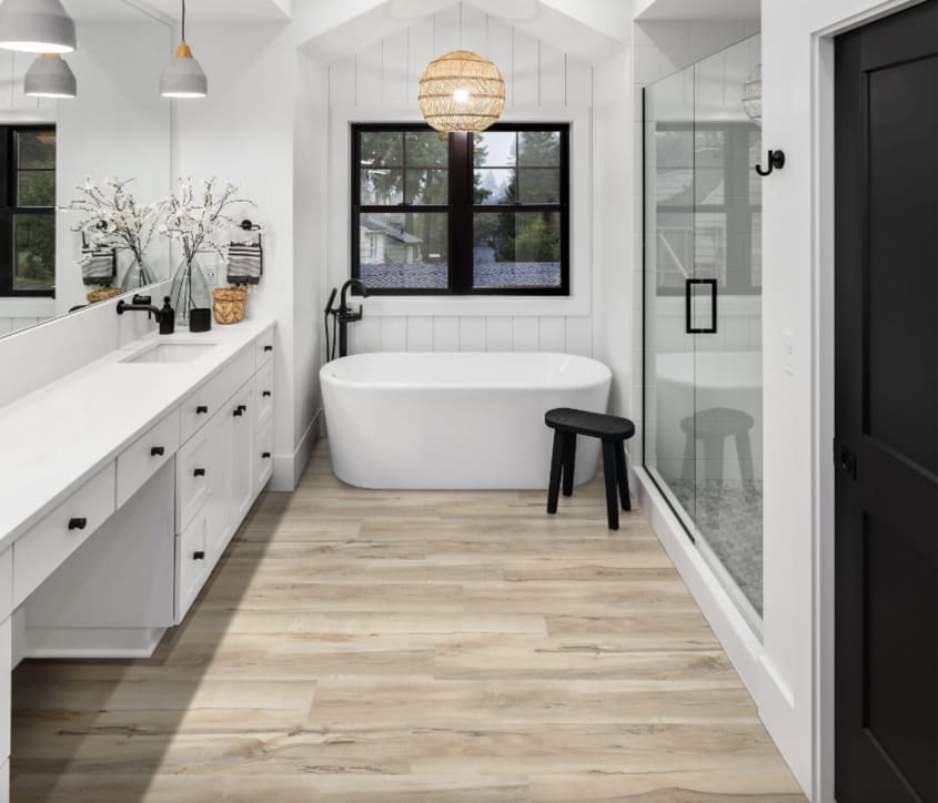 Salle de bain mélangeant les styles farmhouse et japonais, avec baignoire ovale dans une alcôve lambrissée, tabouret de bain, suspension globe en rotin, carrelage en vinyle imitant le bois, meuble-lavabo à plusieurs tiroirs, vaste douche à deux portes vit
