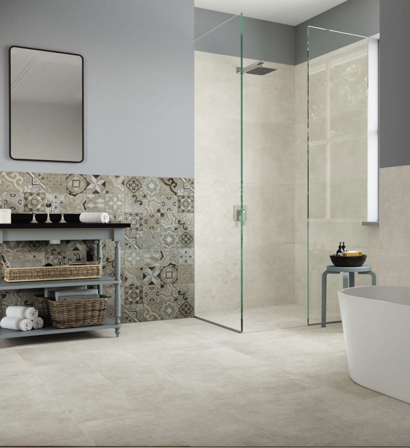 Vaste salle de bain tout en nuances de gris et de beige, comprenant une douche à parois de verre, une baignoire ovale, un petit banc et un meuble-lavabo en bois gris, des paniers en rotin. La douche est parée de carreaux en ciment imitant le marbre, et un