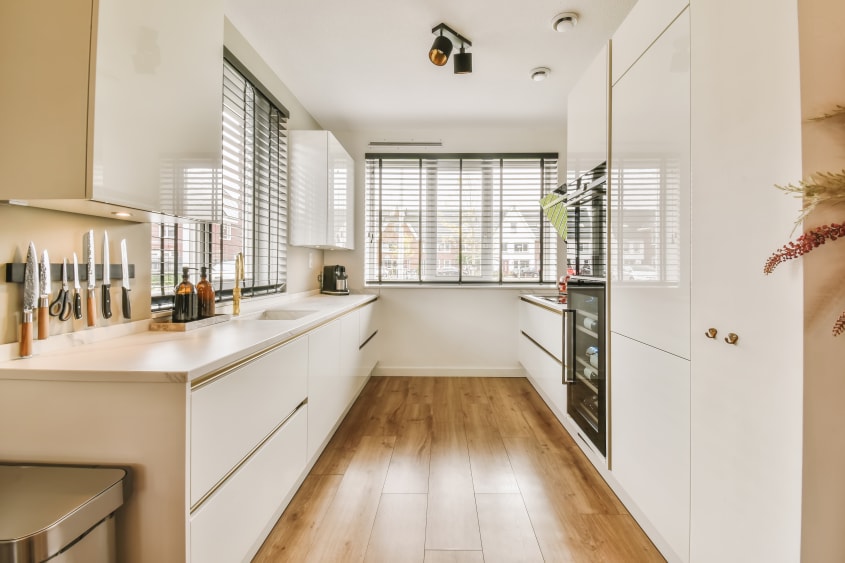 Cuisine minimaliste aménagée en longueur avec armoires blanches et plancher en bois