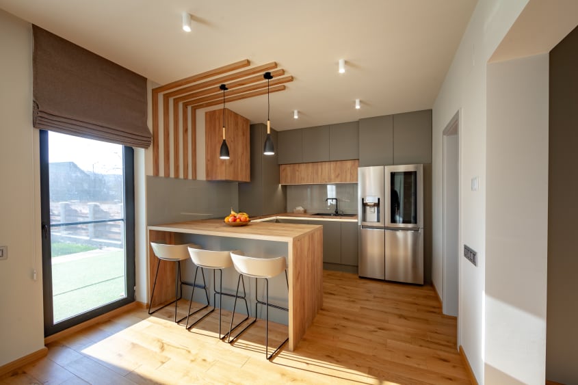 Small minimalist kitchen painted in taupe, with natural wood floor and details, peninsula with three bar stools