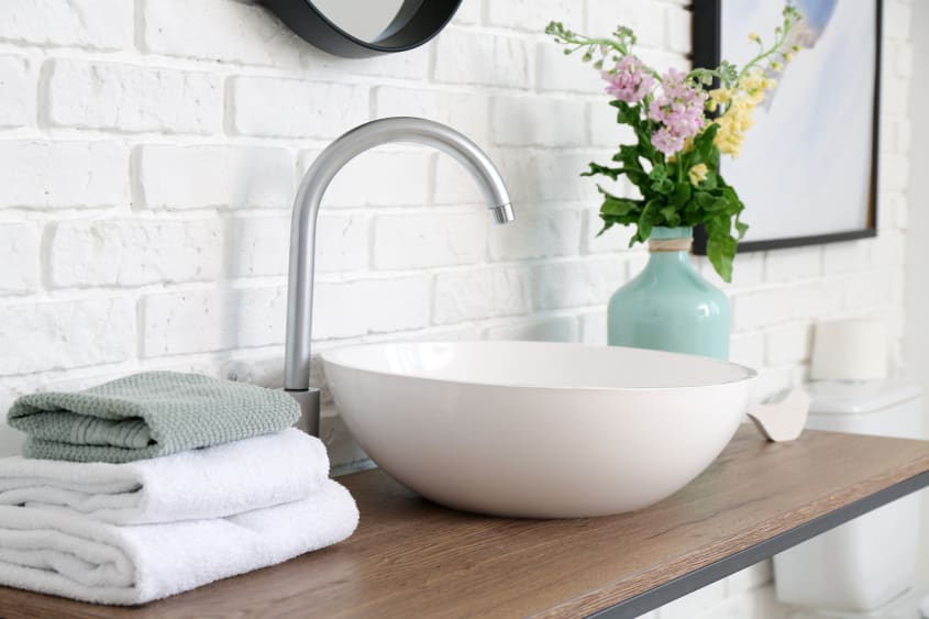 Bathroom with white brick wall, white round vessel sink and silver sink