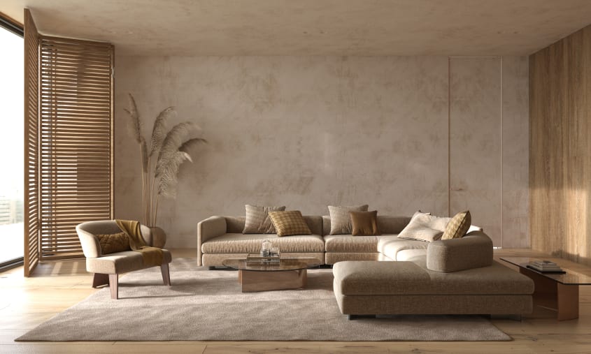Salon monochrome aux tons neutres à mur et plafond en plâtre, canapé modulaire couvert de coussins, fauteuil à dossier arrondi et claustra en bois devant fenêtre