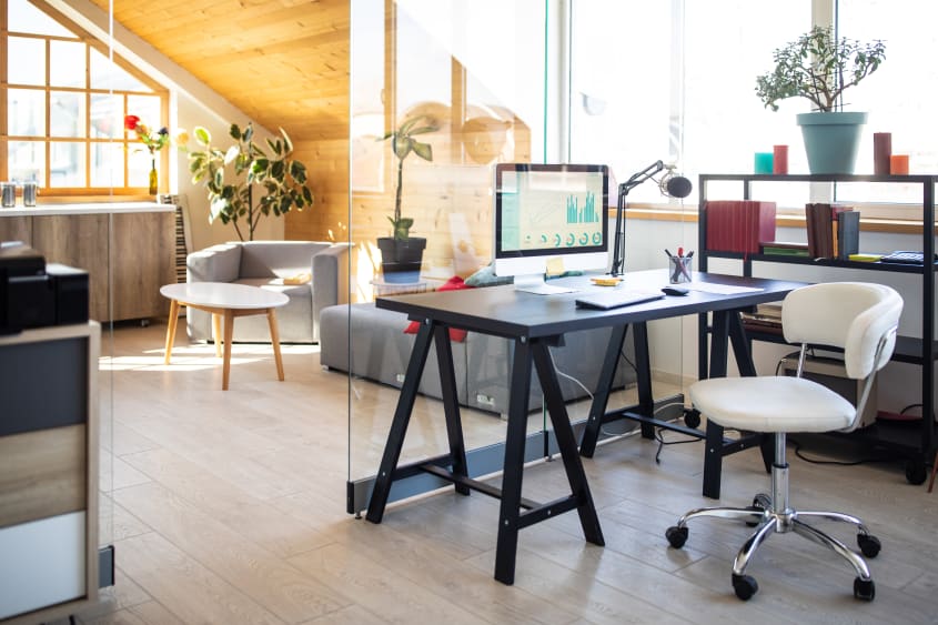 Espace de travail ensoleillé, table à tréteaux et chaise sur roulettes, cloison en verre pour séparer le coin de lecture avec fauteuil carré et table basse