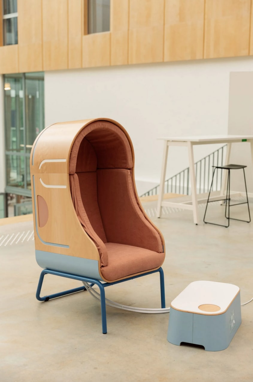 Fauteuil à coque en bois et coussins gonflables à l’intérieur, et repose-pieds, placés dans un grand espace de bureau