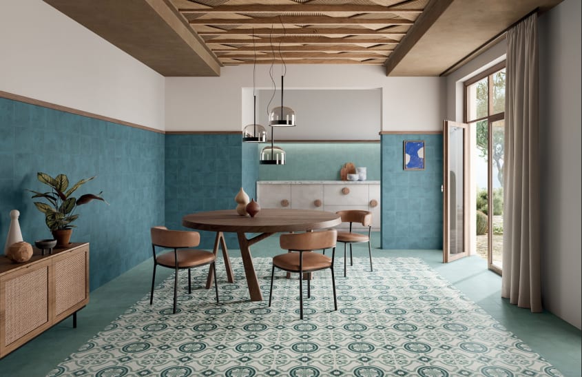 Salle à manger aux murs décorés de tuiles bleues, carrelage au sol à motifs fantaisie, table en bois et chaises en cuir brun, bahut avec portes en cannage de rotin