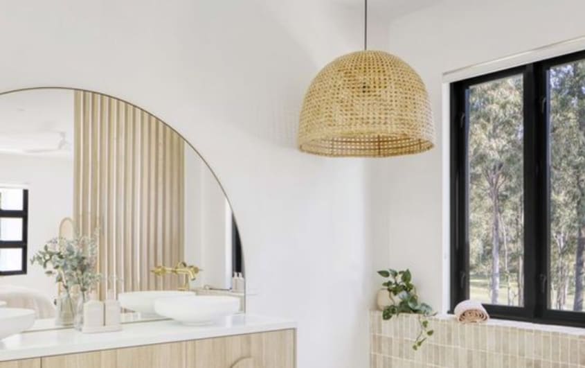 Salle de bain avec un meuble-lavabo en bois et un miroir en demi-cercle et un lustre en rotin au-dessus de la baignoire