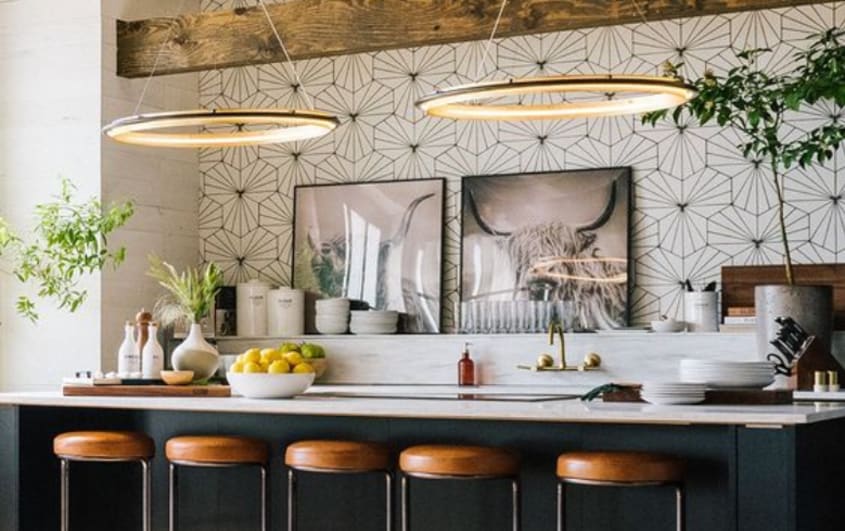 Cuisine de style bar avec tabourets, deux grands lustres, îlot noir et dosseret en mosaïque.