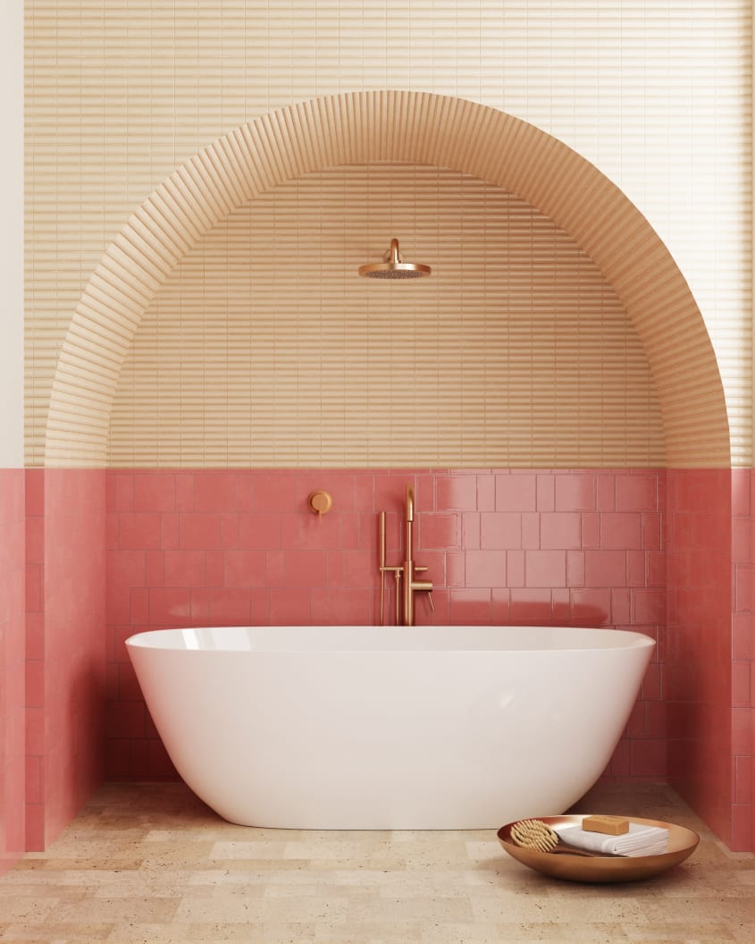 Dans une salle de bain de luxe, baignoire autoportante blanche dans une alcôve en arche avec mur orné à moitié de carreaux en céramique glacée couleur frappé à la fraise, l’autre moitié en tuiles étroites couleur biscuit, plancher en travertin et plateau 