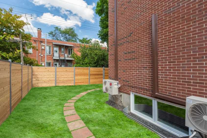 aménagement extérieur d'un duplex récemment agrandi - vue sur le côté avec gazon, pas de béton et clôture en bois