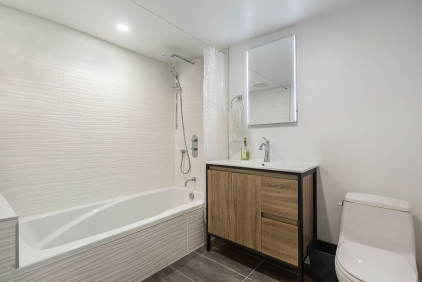 salle de bain moderne rénovée au sous-sol avec vanité en bois, bain et toilette