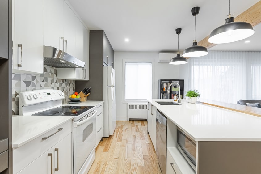 Cuisine à aire ouverte moderne avec armoires blanches et grises, îlot et comptoirs de quartz blancs