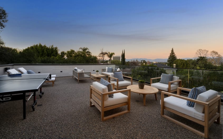 Toit terrasse avec garde-corps en verre, coucher de soleil, mobilier en bois pâle avec coussins crème, table de ping-pong