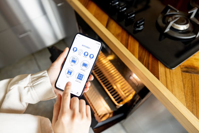 Femme tenant un téléphone avec une application de maison intelligente, contrôlant les appareils de cuisine à distance