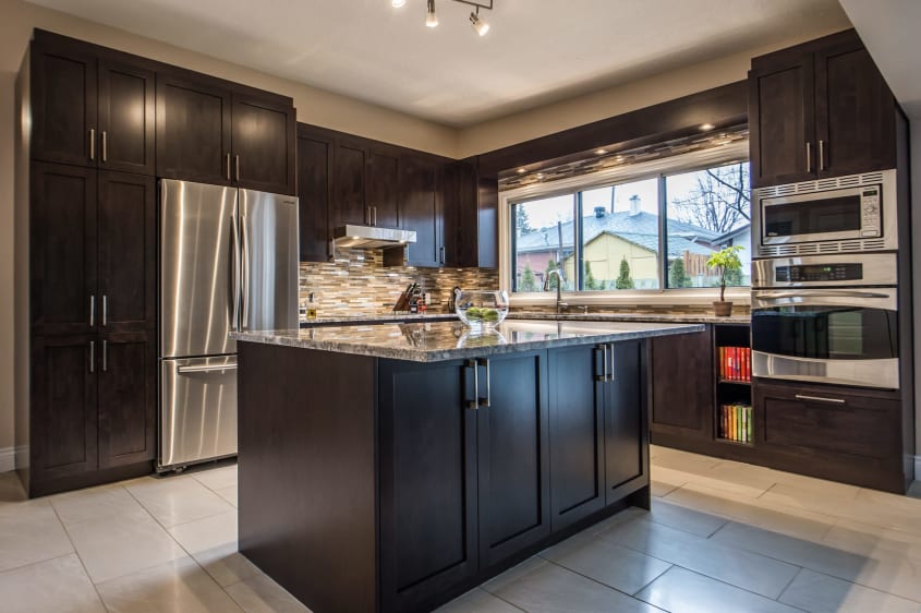 cuisine moderne en bois foncé de style shaker avec îlot, comptoirs de granite et four encastré